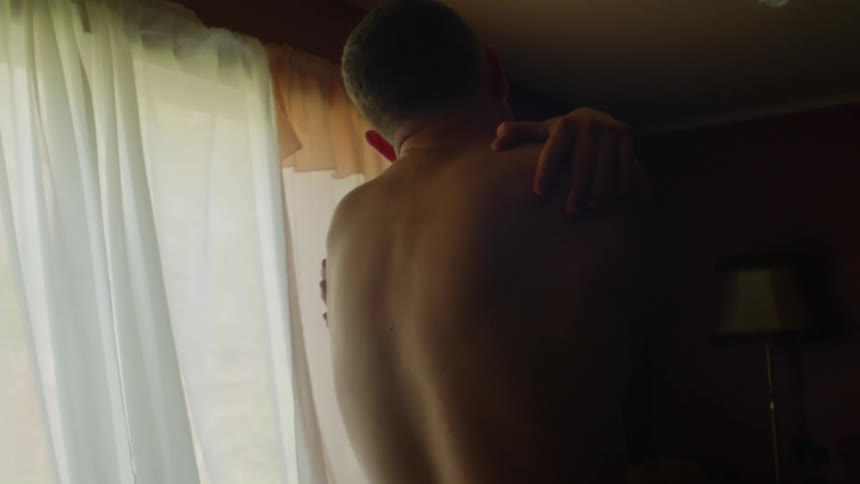Young shirtless man rubs his chest and moves frantically inside a dimly lit room