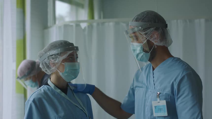 Doctor and nurse wearing personal protective gear talking on a hospital room