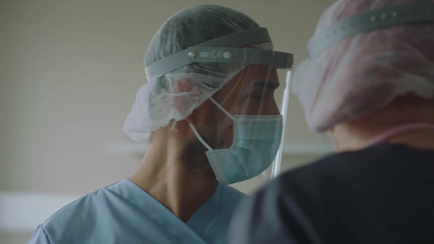 Two doctors wearing face masks and shields talking in a hospital room