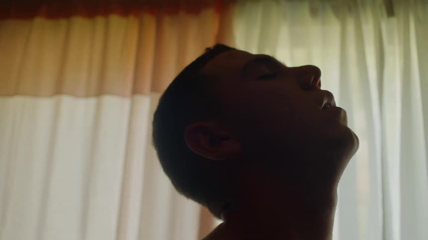 A man in a room with a wall a window and curtains in the background