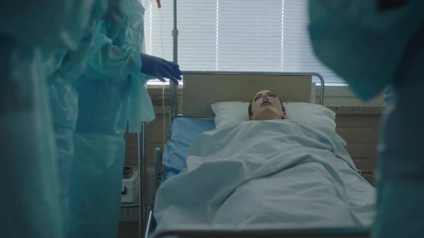 A woman laying in a hospital bed surrounded by five nurses with gloves and masks
