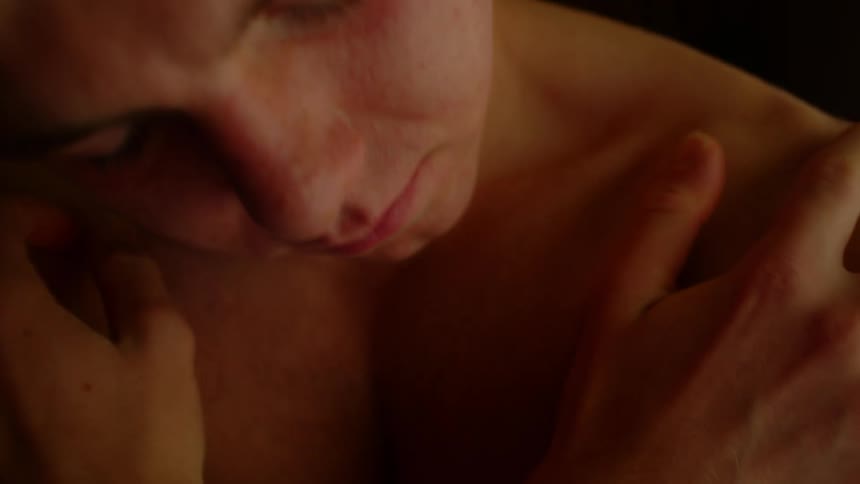 Young shirtless man rubbing his arms and chest inside a dimly lit room at home