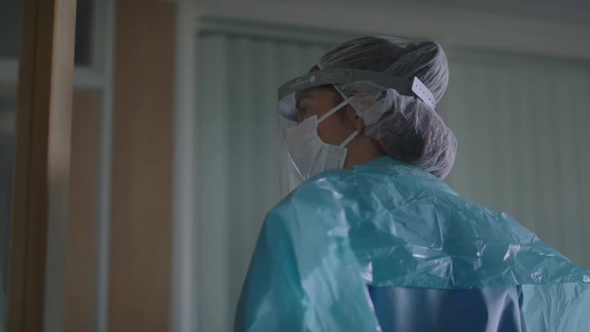 Nurse wearing scrubs and protective gear pauses to observe then rushes through door