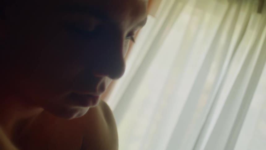 Young shirtless tired man hugs himself inside a dimly lit room at home