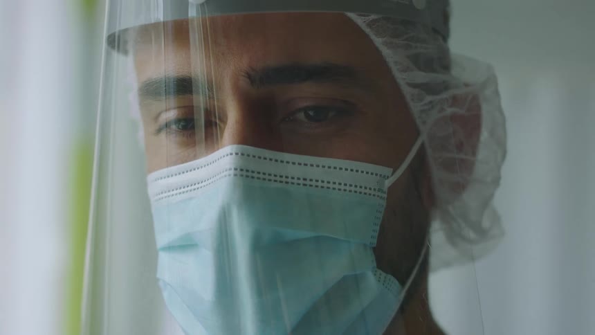 A man is wearing a surgical mask and a plastic shield on his face