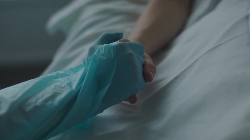 Medical personnel holds hand of patient lying in hospital bed