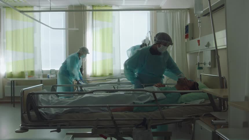 Nurses wearing hospital scrubs are taking care of patients in a hospital room