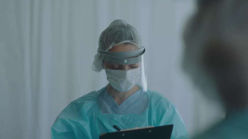 A medical worker writes on a clipboard in a hospital while wearing personal protective equipment