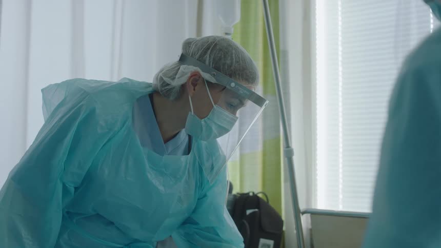 Two nurses with masks and face shields in the hospital room with a window in the background