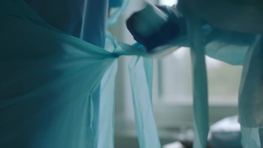 A nurse ties a plastic coverall over the scrubs of another nurse