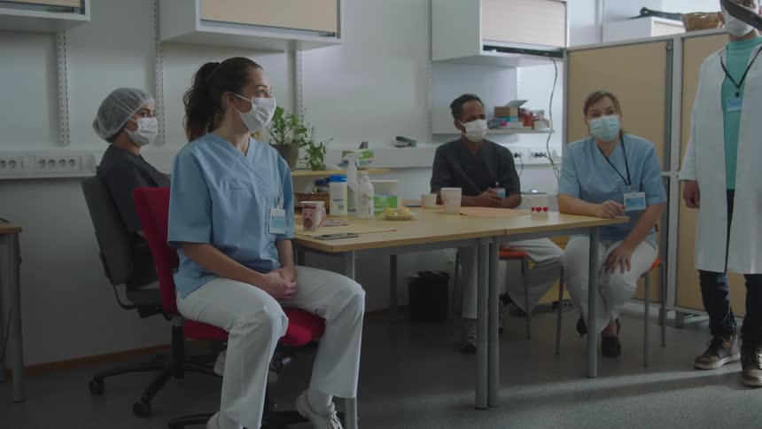 Medical team meet in break room around table listening as one references clipboard