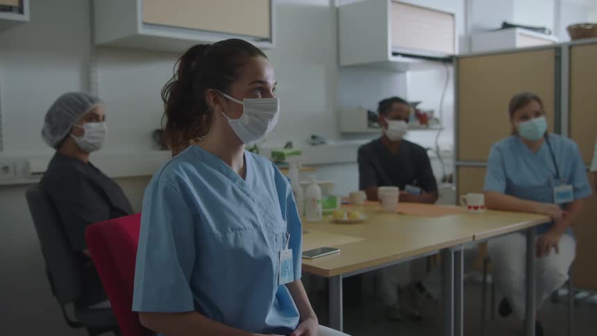 Nurse wearing a face mask sitting with coworkers on a meeting room at the hospital