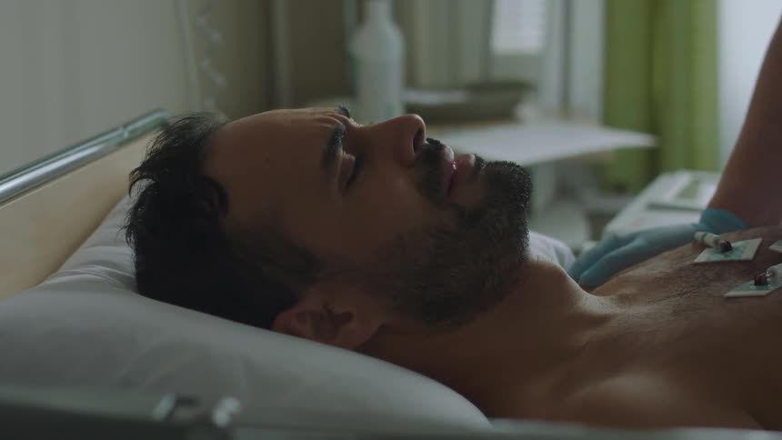 A man laying in a hospital bed with another person with gloves touching his shoulder