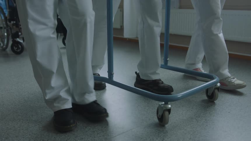 Medical personnel help patient walk using wheeled walker