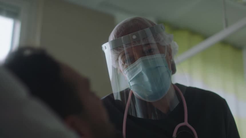 Doctor wearing protective equipment talking to a patient layin in a hospital bed
