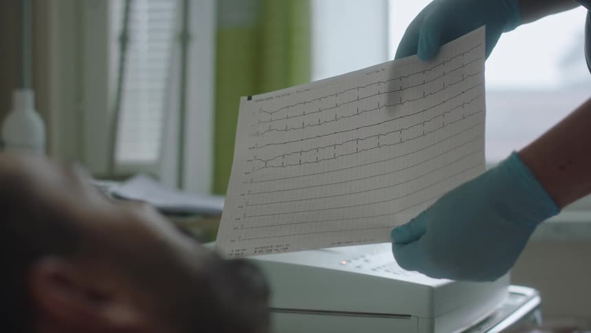 A nurse is showing a male patient a medical chart as he is laying in bed in a hospital