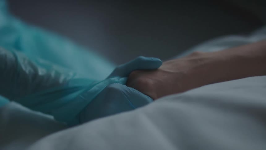 A nurse wearing blue scrubs holds the hand of a patient