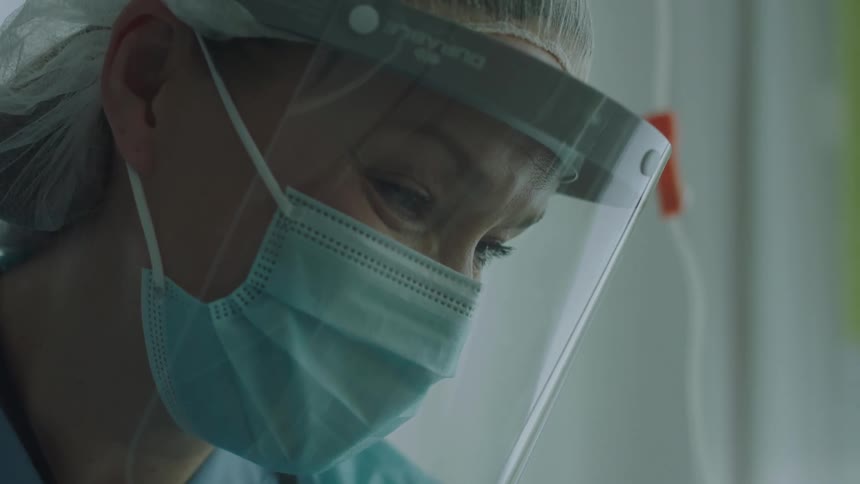 A nurse with ppe on is looking down and nodding