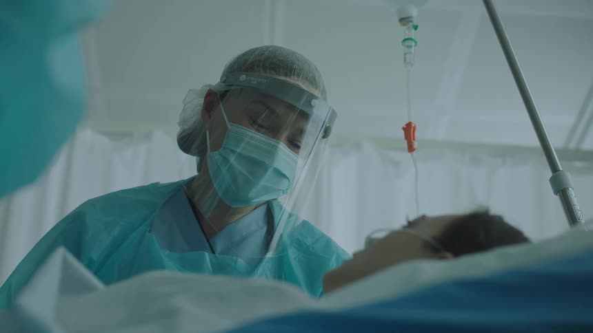 Nurse wearing face shield and mask talking to a patient laying on a hospital bed