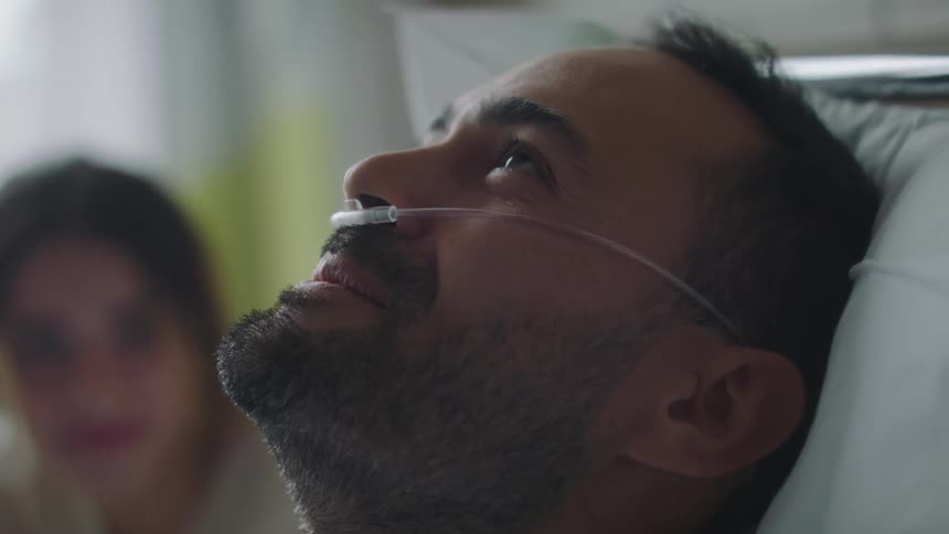 A man in a hospital bed leans back and smiles while talking to a family member