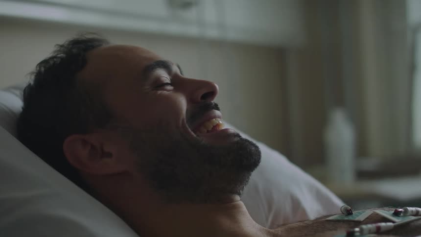 A man is laughing in the hospital bed
