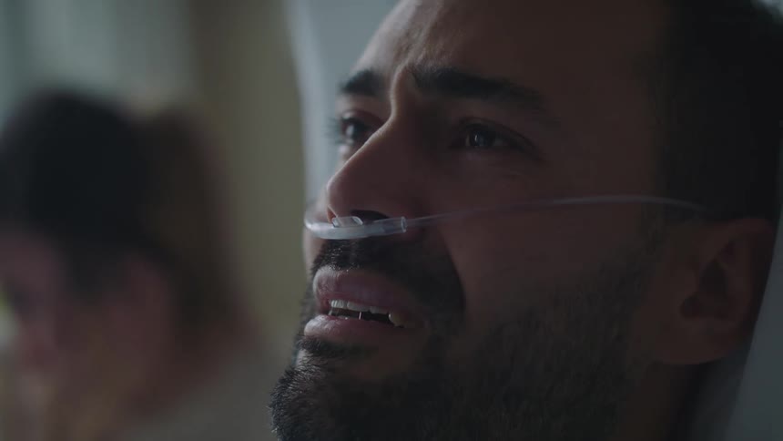 Man sitting in a hospital bed with a nasal cannula crying near his sad wife