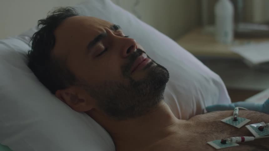 A person with a gloved hand rubs the shoulder of a patient in a bed with an ekg monitor