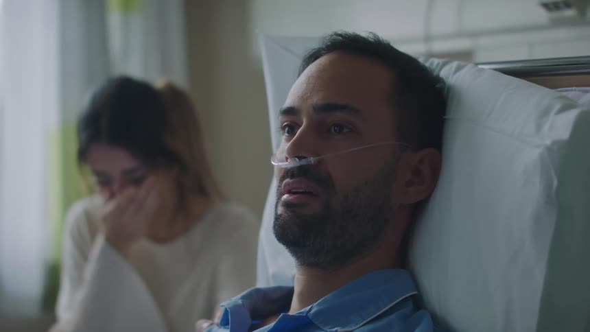 Woman crying near a patient laying in a hospital bed with a nasal cannula