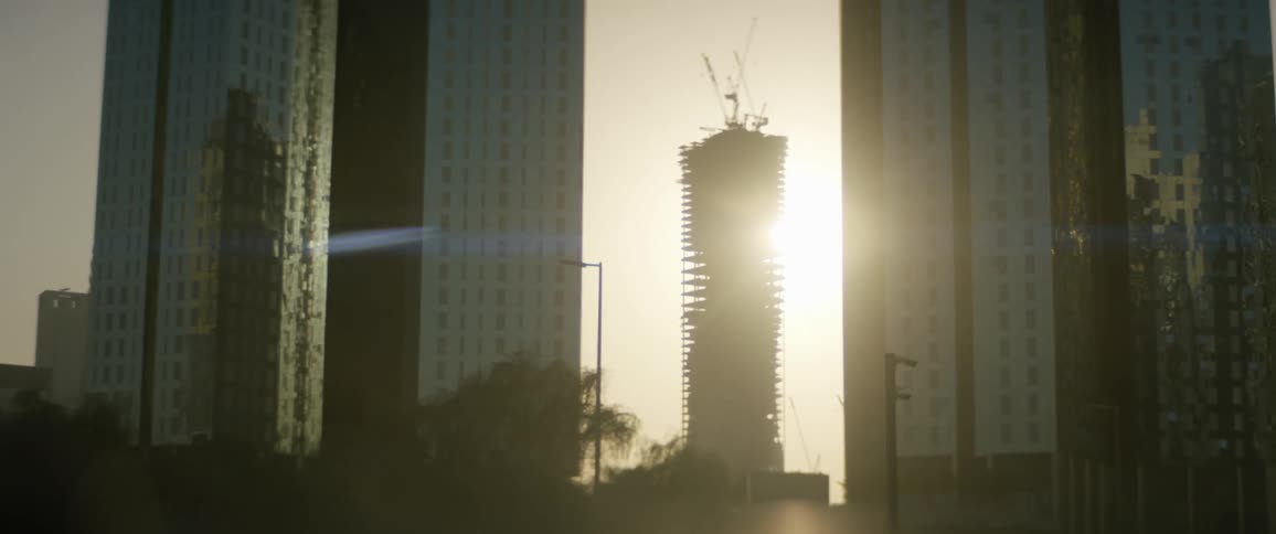 The sun is setting behind two skyscrapers with another skyscraper being constructed in the distance