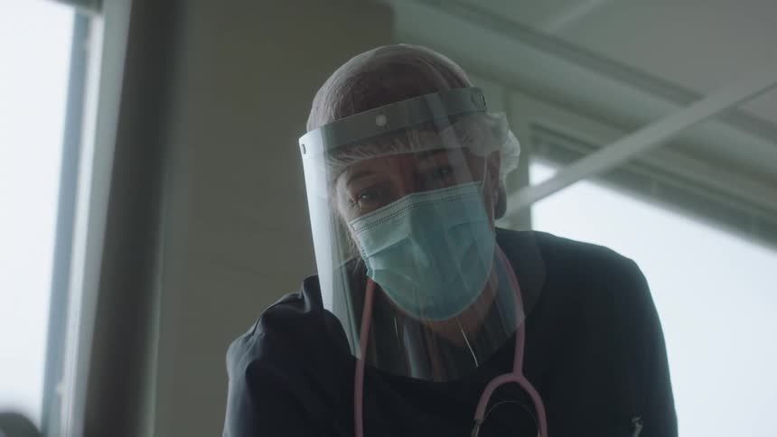 A woman with a mask a face shield a stethoscope and scrubs