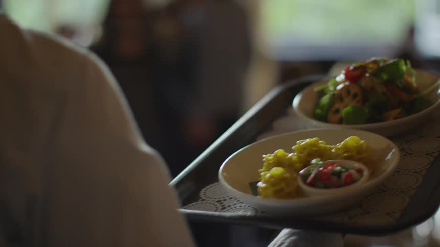 A server carries a tray with two meals on it to a table in a crowded restaurant