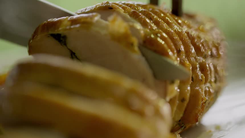 A carving fork holds a round stuffed pork roast as a knife slices through