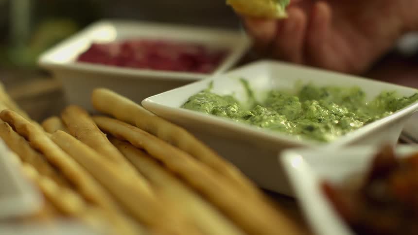 Hand dipping a piece of bread on a dish filled with guacamole