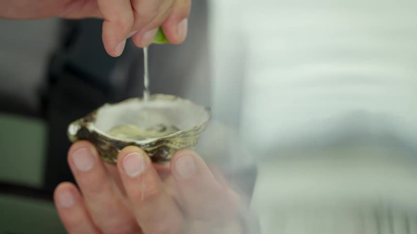 Cook wearing apron squeezes lime juice onto oyster in half shell