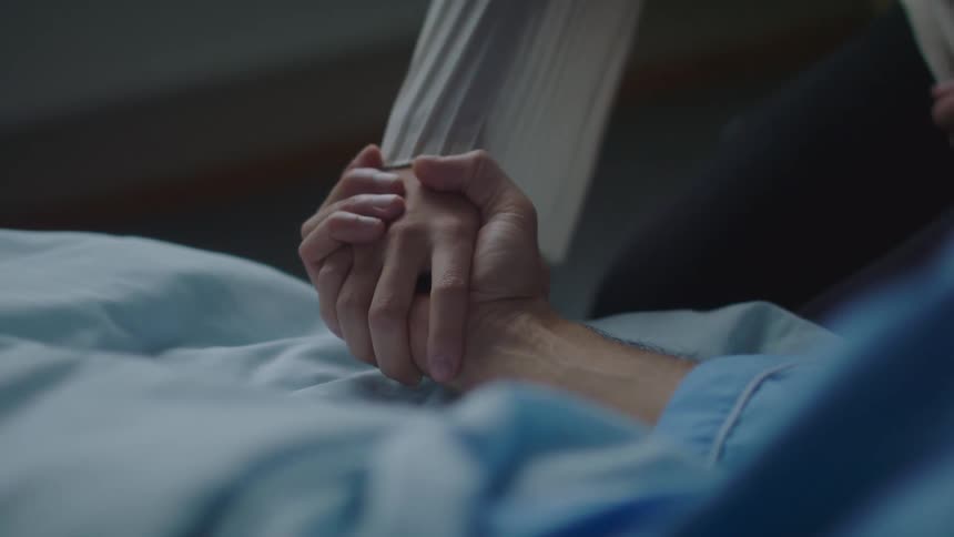A visitor holds the hand of a hospital patient