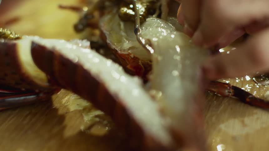 A person is opening a cut lobster on a cutting board