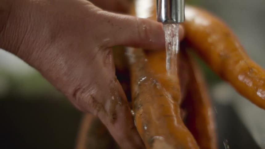 Hand rubbing carrots under the kitchen sink to wash them