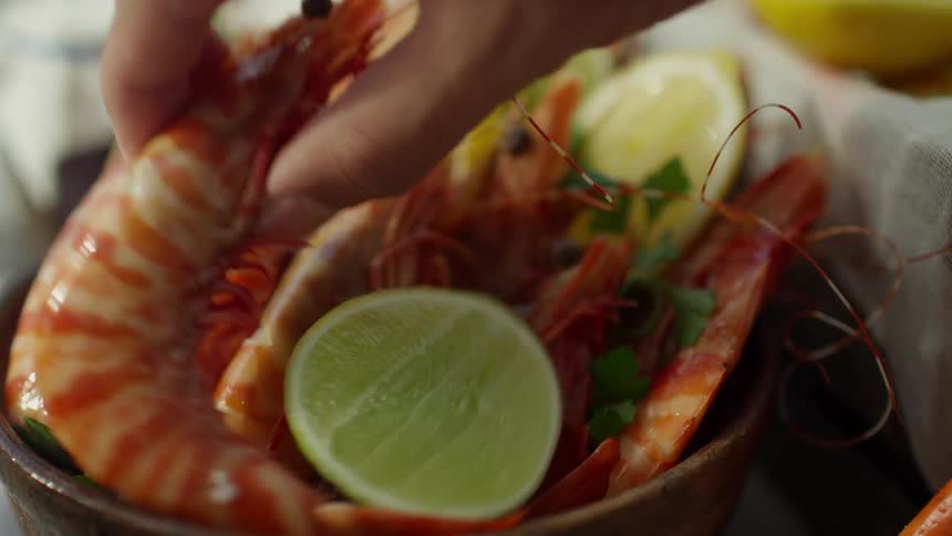 Person picks up unshelled cooked shrimp from bowl garnished with lemon and lime slices