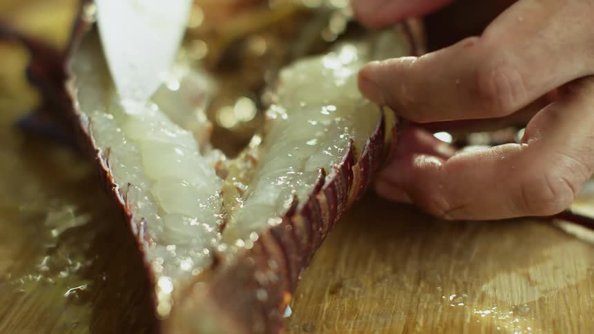Person splits cooked lobster in half on wooden surface