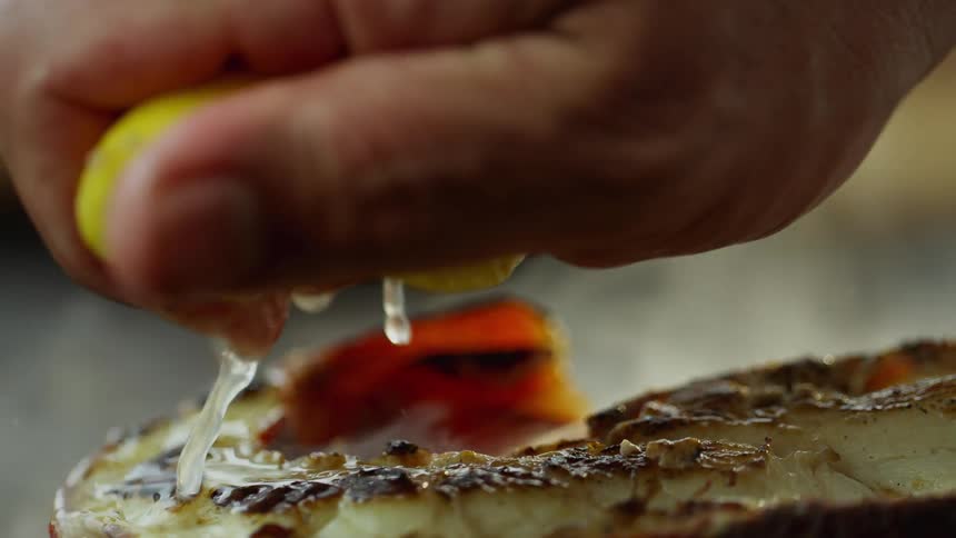 Hand squeezing fresh lemon juice over sliced lobster over a pan
