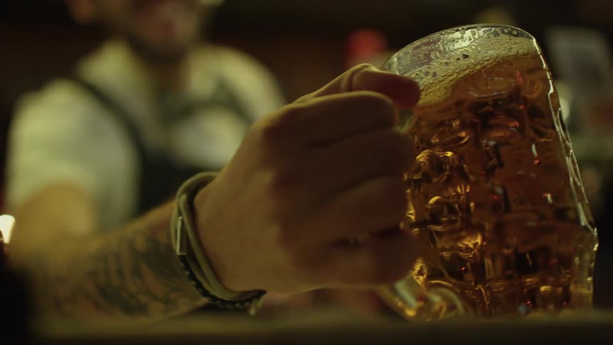 A man smiles as he sets a mug of beer down near beer taps