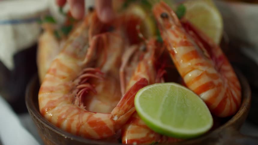 Close up of hands picking up cooked large shrimp from a bowl