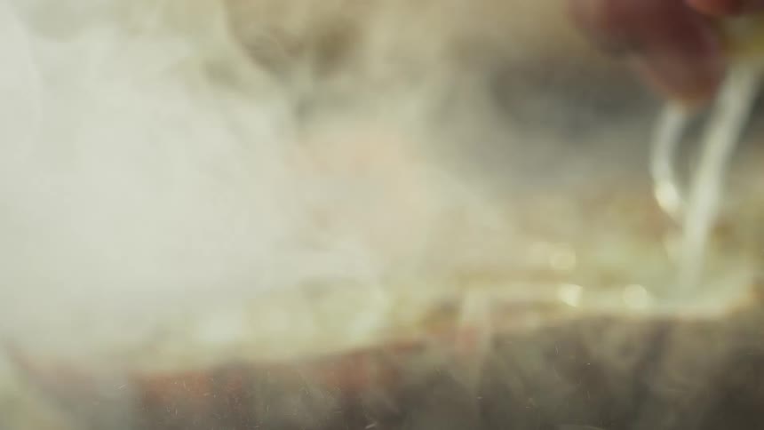 Chef squeezes citrus juice onto cooking seafood half causing smoke to rise from grill