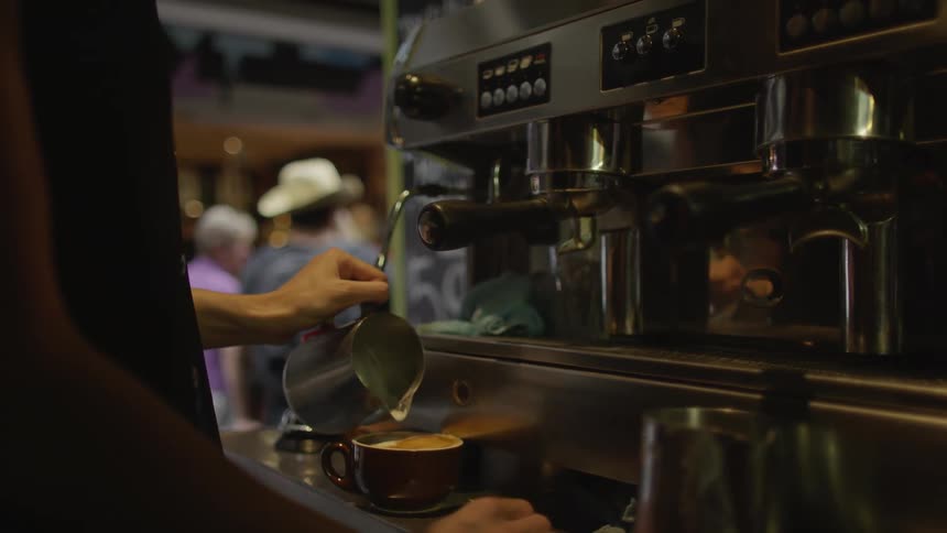 A barista pours frothed milk into a cup as people pass by