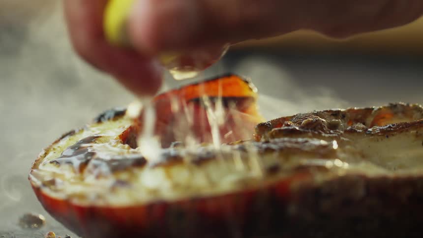 Hand squeezing lemon over a lobster shrimp while its cooking