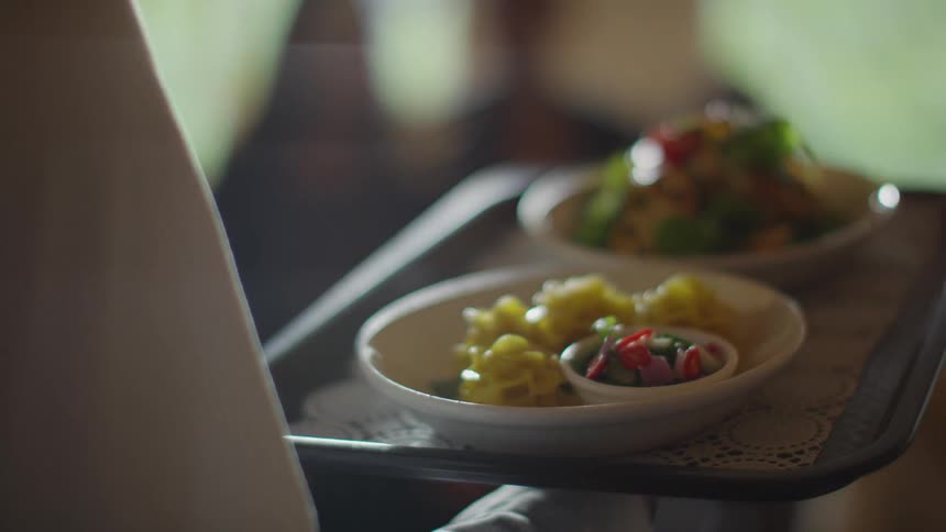 A waitperson carrying a tray with two plates of food on it is approached by two customers