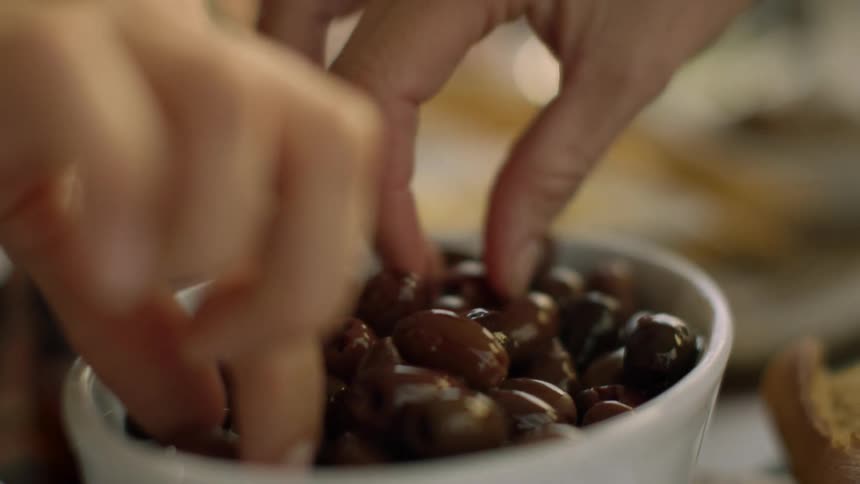 Two people picking up black olives from a white ceramic bowl