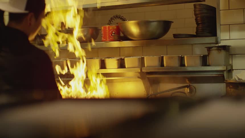 Chef cooking on a restaurant stirs food on fire over the kitchen range