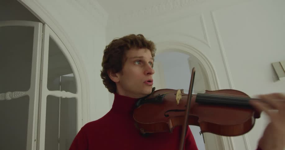 A man plays the violin while standing next to an arched doorway at home