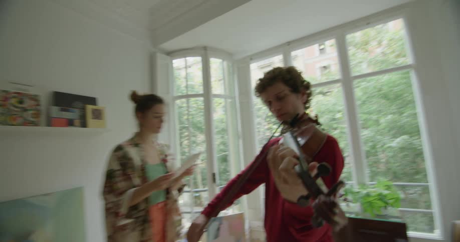 Woman teaching a young man how to play violin in an apartment